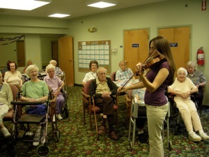 Kristin playing violin for an audience of seniors in a community room